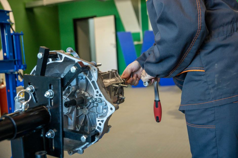 Mechanic uses tools to repair car transmission in an indoor workshop setting.